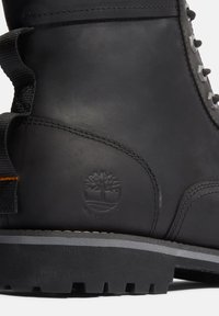 Zwarte waterdichte laars met een textuur leren bovenkant, grijze rubberen zool, gestikte accenten en een op de zijkant geperste logo.