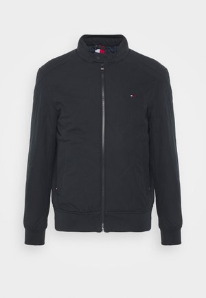 Schwarze gesteppte Jacke mit Frontreißverschluss, Stehkragen, gerippten Bündchen und Saum sowie kleinem rot-weiß-blauem Logo auf Brust und Taschen.