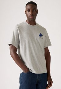 Grijze katoenen t-shirt met korte mouwen en een ronde hals. Bevat een blauw logo en tekst op de linkerborst. Casual pasvorm.