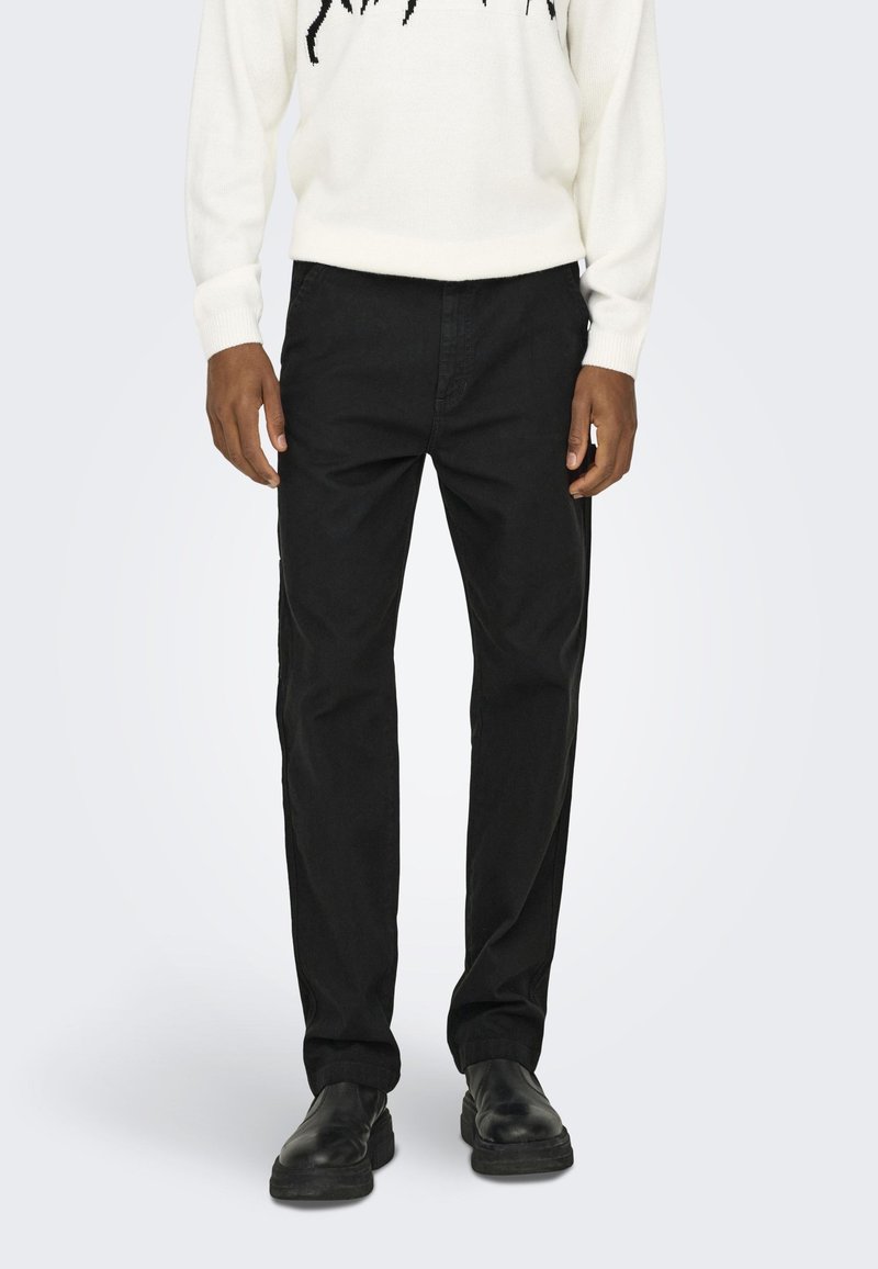 Pantaloni neri in cotone con design a gamba dritta. Presentano tasche laterali e una finitura pulita. Indossati con un maglione bianco.