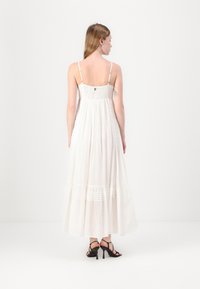 Rochie maxi albă cu bretele subțiri, bust plisat și fustă în mai multe niveluri. Are o textură fluidă și cusături orizontale subtile la tiv.