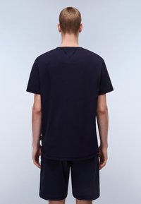 Mørkeblå bomulds t-shirt med korte ærmer, rund halsudskæring og et enkelt design; har en let buet kant bagpå. Mørke shorts.