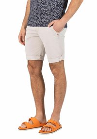 Light beige shorts with rolled cuffs, featuring side pockets and subtle stitching details, paired with bright orange sandals.