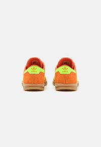 Adidas sneakers with an orange suede upper and bright green accents, featuring a translucent gum sole and logo on the heel.