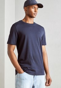 Marinblå kortärmad t-shirt i mjuk bomull med rund krage och subtil logotypdetalj. Bärs tillsammans med ljusblå denimjeans.