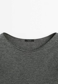 Pull gris en tricot avec un col rond, présentant une texture subtile et une étiquette au col portant l'inscription "Marrone D'oro".