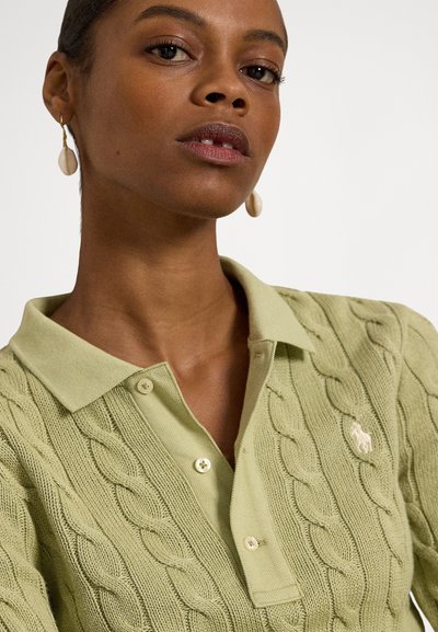 Svetlo zelena polo majica z vzorcem pletenja kabla, ovratnik, dva gumba in majhen logotip. Model nosi krem uhane.