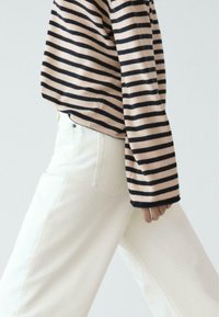 Maglione a righe con linee orizzontali rosa e nere, dalla vestibilità ampia. Abbinato a jeans bianchi a gamba dritta con dettaglio sulla tasca posteriore.