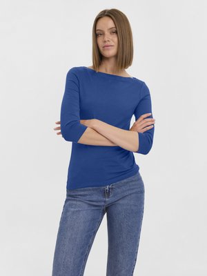 Haut bleu à manches longues avec un col rond, design ajusté et texture douce. Associé à un jean en denim bleu clair.
