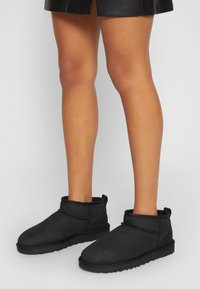 Bottines en daim noir avec un bout arrondi, doublure en fourrure, profil bas et un accent cousu le long du bord supérieur. Semelle en caoutchouc.