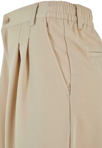 Pantalons khaki avec une taille élastique, présentant des plis sur le côté et une coupe droite. Tissu lisse avec un design simple et un minimum de détails.