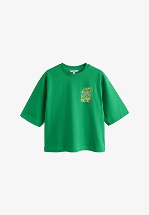 Zelené tričko s krátkým rukávem s barevným potiskem krabičky citronové šťávy na levé straně hrudi, zdobené květinovými a ovocnými motivy.