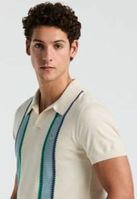 Beige poloshirt met korte mouwen, voorzien van verticale strepen in groen, blauw en lichtblauw; inclusief klein logo op de borst.