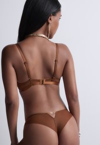 Ensemble de lingerie marron comprenant un soutien-gorge sans couture avec des bretelles réglables et une culotte assortie, mettant en avant une texture lisse et un design minimaliste.