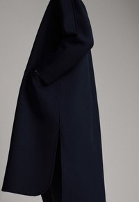Cappotto in misto lana di colore blu navy con una silhouette lunga e dritta, tasche laterali e uno spacco all'orlo per una maggiore libertà di movimento. Tessuto morbido.