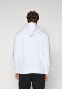 White hoodie with a kangaroo pocket, ribbed cuffs and hem, and a drawstring hood. The fabric appears soft and textured, suitable for casual wear.