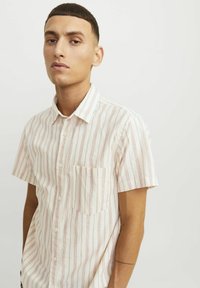 Camisa de botón de manga corta en beige claro con rayas rojas verticales. Cuenta con un bolsillo en el pecho izquierdo y una tela suave y texturizada.