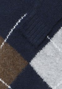 Gros plan d'un pull en tricot multicolore avec un poignet bleu marine, un motif losanges marron et gris, et des détails de couture blancs.