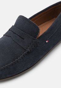 Granatowe zamszowe mokasyny z przeszyciem moc toe, paskiem penny, beżowym wykończeniem wnętrza oraz małym detalem w postaci flagi w kolorach czerwonym, białym i niebieskim po bokach.