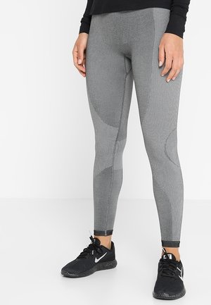Harmaat legginssit, joissa on teksturoitu kuvio ja sileä kangas, verkkoyksityiskohdat ja tiukka muotoilu. Yhdistetty mustien urheilukenkien kanssa.
