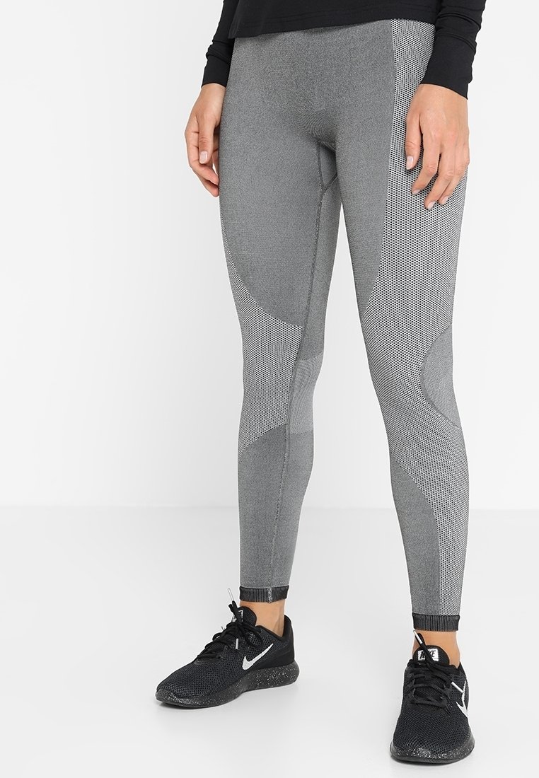 Leggings grises con un patrón texturizado y tela suave, con acentos de malla y un diseño ajustado. Llevados con zapatillas deportivas negras.