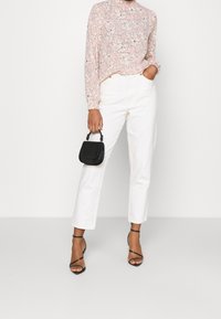 Blommig långärmad topp i rosa med svarta detaljer, kombinerad med vita raka jeans och svarta sandaler med remmar. Svart handväska med handtag.