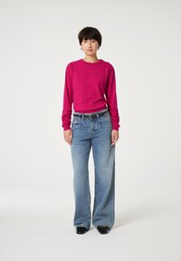 Fuchsia lange mouw top met geplooide details, gecombineerd met lichtblauwe wijde jeans. Een zwarte riem en schoenen maken de outfit compleet.