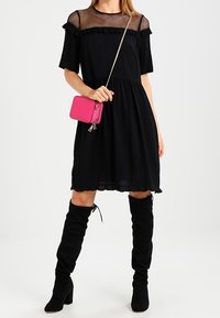 Černé šaty s krajkovým vrchním dílem a volánkovými detaily, mají vypasovaný pas a rozšířenou sukni. Vybavené malou růžovou crossbody taškou a černými vysokými botami ke kolenům.
