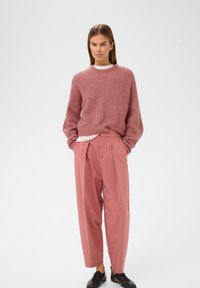 Rosa strikket sweater med rund hals, parret med højtaljede lyserøde plisserede bukser og sorte snørestøvler. Glat tekstur.