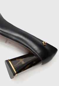 Black leather high-heeled shoe with a tortoiseshell block heel and small gold logo detail near the toe.