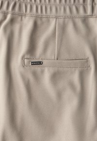 Beige tygshorts med en strukturerad yta, som har en bakficka och är accentuerade med en liten metallisk logotyp.