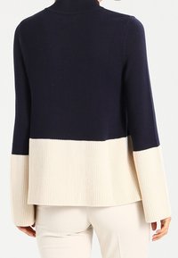 Marineblauer und crèmefarbener zweifarbiger Pullover mit Rollkragen, gerippten Bündchen und geradem Schnitt. Der Saum ist mit einem breiten, gerippten Crèmeabschluss versehen.