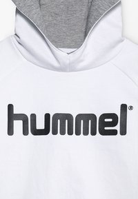 Felpa bianca con cappuccio interno grigio. Presenta un grande logo nero "hummel" sul petto, realizzato in morbido cotone.