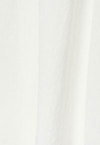 Tissu blanc texturé avec de subtils plis verticaux, montrant un matériau doux et léger.