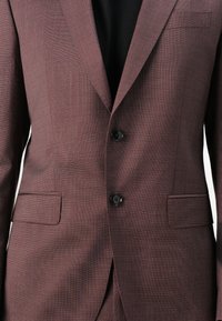 Giacca da abito bordeaux su misura con un motivo testurizzato, due bottoni neri e una tasca sul petto. Presenta rever a becco e un design slim fit.