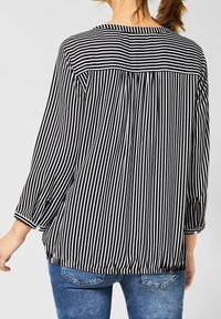 Schwarz-weiße gestreifte Bluse mit Dreiviertelärmeln, lockerer Passform, Knopfdetails an den Bündchen, weichem Stoff und gefaltetem Rückendesign.