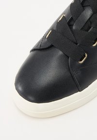 Sneaker in pelle nera con punta arrotondata, tomaia testurizzata, lacci neri piatti e occhielli dorati, con suola in gomma bianca.