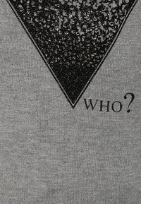 Sweatshirt gris avec un grand design de triangle noir pailleté et une surface texturée, et le mot "WHO?" en texte noir gras en dessous.