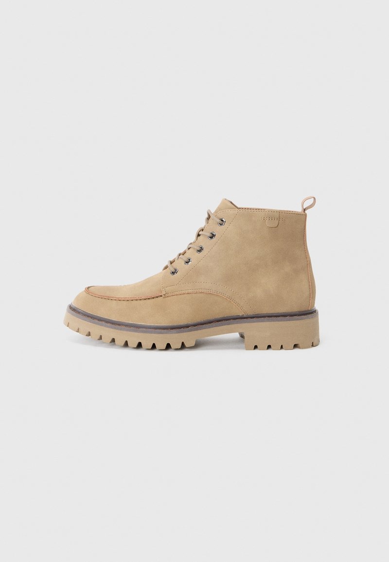 Bottine à lacets en daim couleur fauve avec semelle robuste, bout rond et languette au talon, vue de profil sur fond uni.