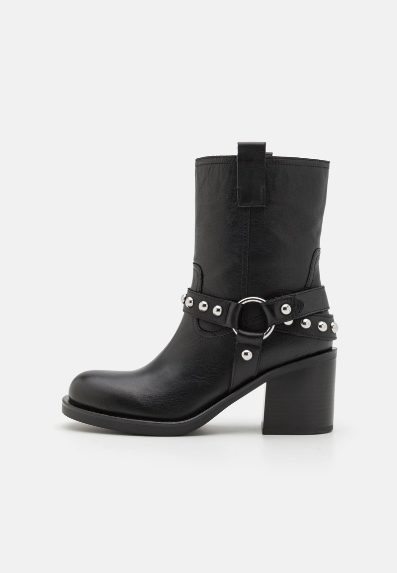 Czarne skórzane botki do kostki na wysokim słupku, z paskiem ozdobionym srebrnymi ćwikami i metalowym detalem w kształcie pierścienia.