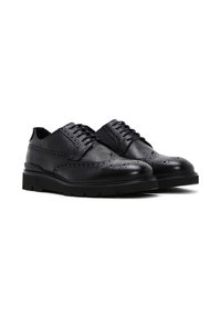 Chaussures en cuir noir avec des détails en brogue, présentant une texture lisse, un bout rond et une semelle en caoutchouc noir solide pour une bonne adhérence.