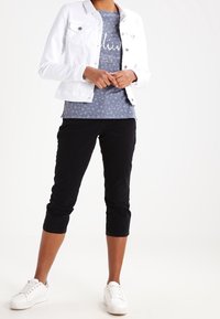 Chaqueta de mezclilla blanca, camisa gris con estampado floral y texto, pantalones capri negros y zapatillas blancas. Conjunto ligero y casual con texturas en capas.