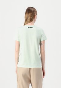 Lys grøn bomulls t-skjorte med korte ermer. Har en rund hals og en svart logo bak. Glatt tekstur, avslappet passform.