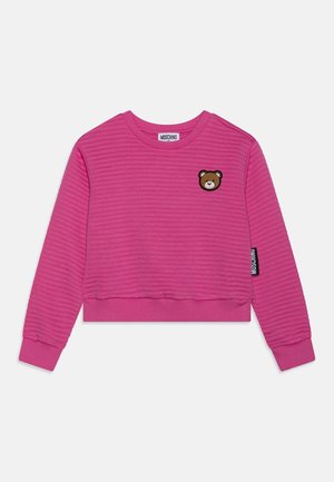 Sweat-shirt à manches longues côtelé rose vif avec un petit patch ours brun sur la poitrine et une étiquette logo Moschino sur le côté.