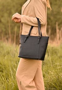 Sac tote en cuir noir avec deux poignées, forme rectangulaire, poches latérales et accents en métal argenté. Texture lisse, design minimal.