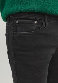 Jeans de mezclilla negra con una textura suave, con remaches plateados, cinco bolsillos y un diseño clásico de cinco bolsillos.