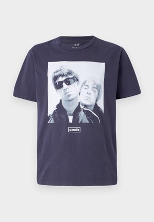 T-shirt de algodão azul-marinho com uma grande impressão gráfica de duas figuras masculinas. O texto "oasis" está centralizado abaixo da imagem. Manga curta, decote redondo.