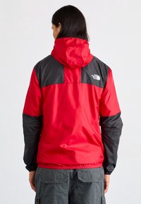 Czerwona i czarna kurtka przeciwdeszczowa z kapturem, elastycznymi mankietami i dołem. Zawiera logo na górnej części pleców. Gładki, lekki materiał.