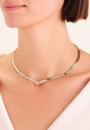 Collana di tonalità argento con un design flessibile e testurizzato a forma di V e un moschettone centrale, posata su un collo nudo.