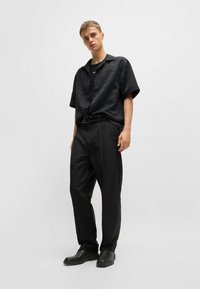 Camisetta nera a maniche corte con un motivo sottile, abbinata a pantaloni larghi neri e scarpe nere. I capi presentano una vestibilità comoda e una texture morbida.